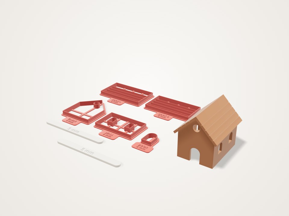 Set of coral cutters for walls, gables, roof and door beside a small assembled house, with two flat guide sticks